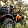 Pilote de quad orange casqué, de dos, sur un sentier en forêt